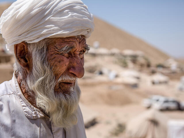 En äldre man står i ett tort landskap i Afghanistan.