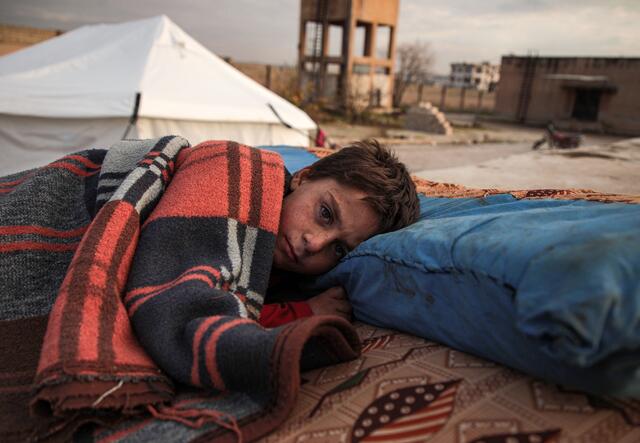 Ett syriskt barn sover under bar himmel i ett flyktingläger