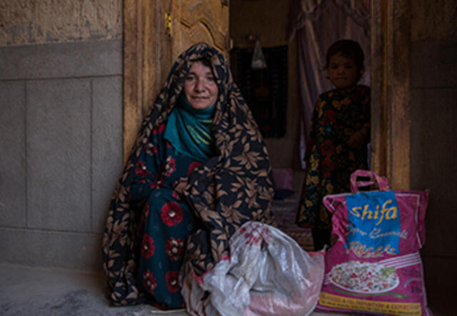Kvinna sitter utanför sitt hus i Afghanistan