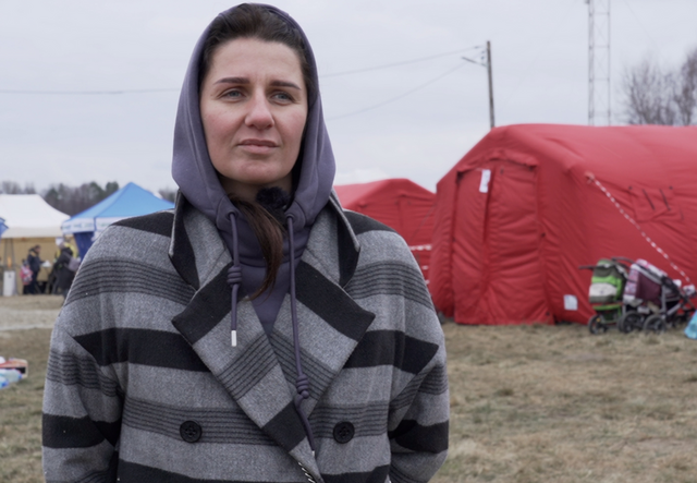 Angelina står utanför några tält på gränsen mellan Ukraina och Polen