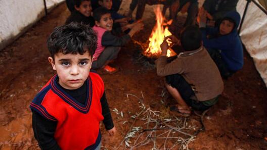En pojke står vid en eld i Syrien och värmer sig